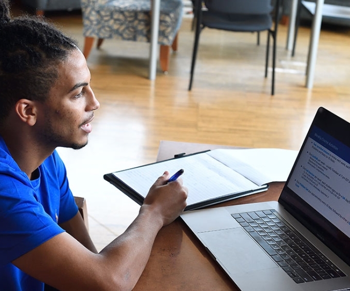 Student in blue shirt on laptop at a table