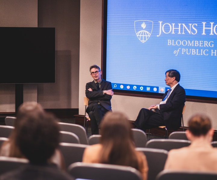 Two men are seated at the front of a lecture hall