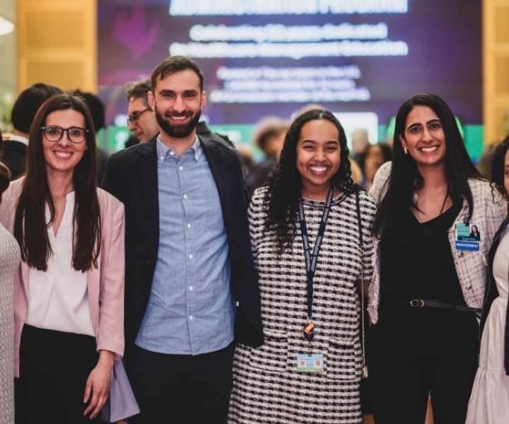 Several young adults wearing business casual outfits stand side by side to smile for a photo