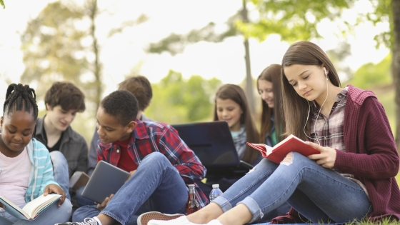 group of middle schoolers sitting on ground looking at books