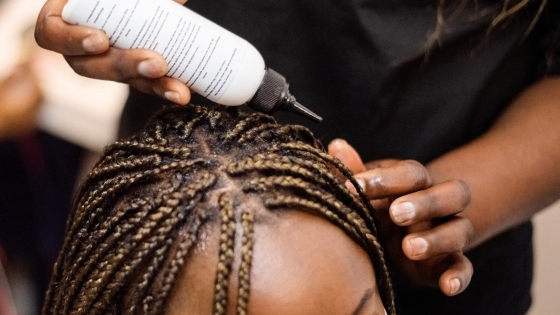 Black hairdresser applying solution to a black female client's head. 