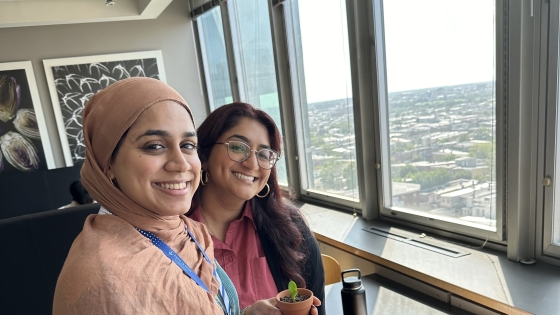 Two Bloomberg School PRFH students smile near a skyline view of Baltimore in the 9th floor cafe.