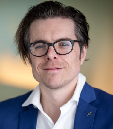 A headshot of Danny Scerpella, a man with a light skin tone, short dark hair, and black glasses