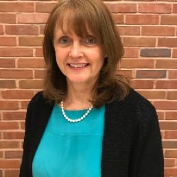Val Culotta stands smiling in front of a brick wall