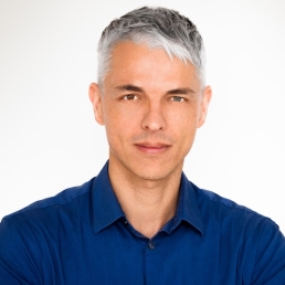 Headshot of Attila Pohlmann, PhD, a man with brown eyes, styled grey hair, a light complexion, and a neutral expression, wearing and a dark blue button-down shirt