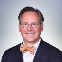 A headshot of a man wearing an orange bowtie and black suit jacket.