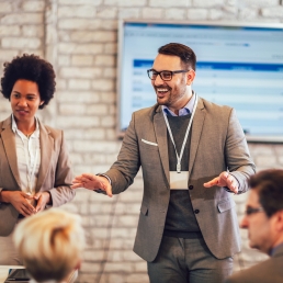 Man with glasses standing, talking to two people sitting in front of him