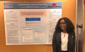 Presenter, Angelease Bunton standing in front of her poster presentation titled, "Overdose Prevention in Injury Prevention Journals."