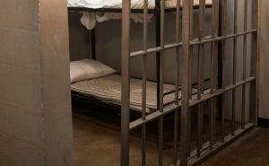 A jail cell with the bar doors opened halfway. A bunk bed is visible behind the bar door.