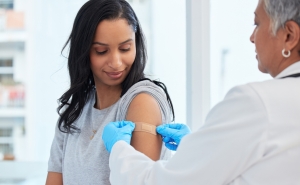 A doctor places a bandaid on a woman's upper arm following vaccination.