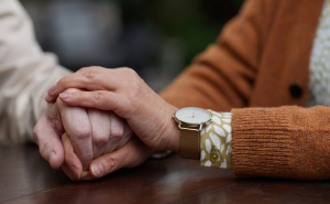 A closeup of two people holding hands at a table. One of the people is younger than the other.