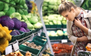 A woman looks at options in a produce section that includes red and green cabbages, onions, tomatoes, and more