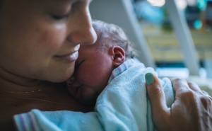 Closeup of mother holding newborn to her chest in hospital bed