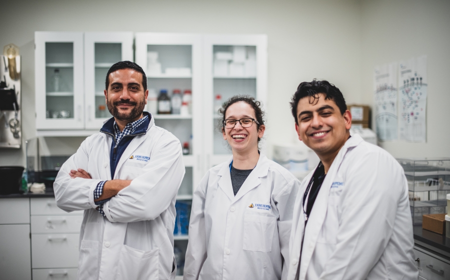 Vito Rebecca and two students stand in lab wearing lab coats