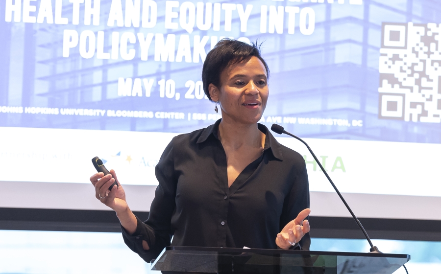 Department Chair Keshia Pollack Porter stands behind a podium and in front of a projector screen as she speaks into the podium microphone.