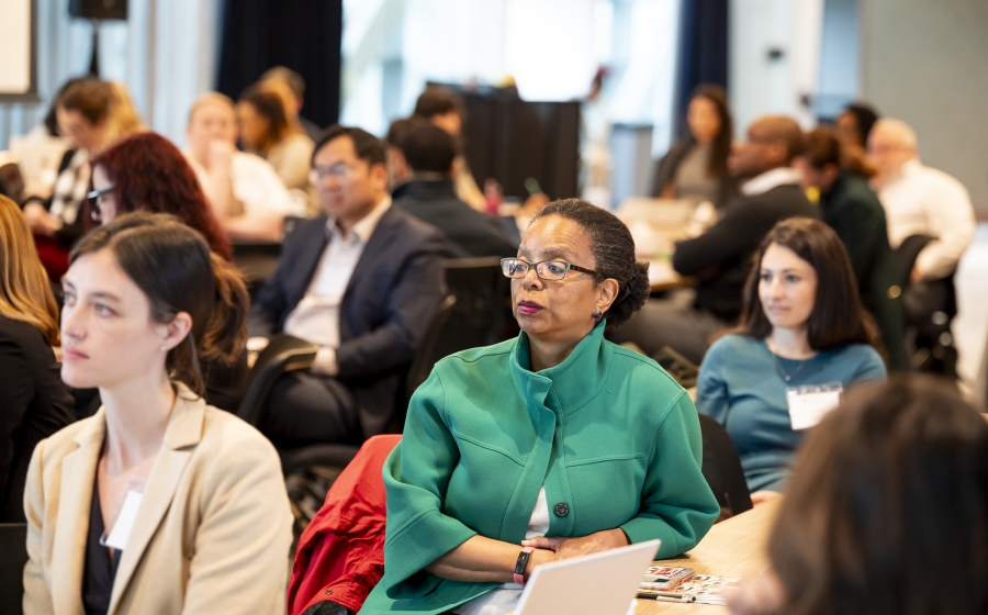 Maryland State Delegate Robbyn T. Lewis seated at one of several wooden long tables facing the front of the room. She's surrounded by fellow attendees by her side and in the background.