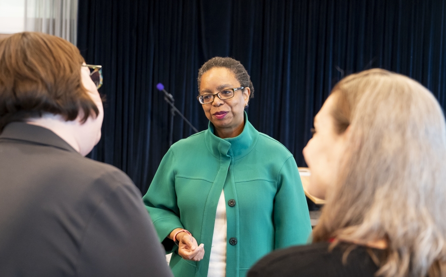 Maryland State Delegate Robbyn T. Lewis is facing the camera and positioned between two women whose backs are facing the camera. Lewis is looking at one of the women with a subtle smile.