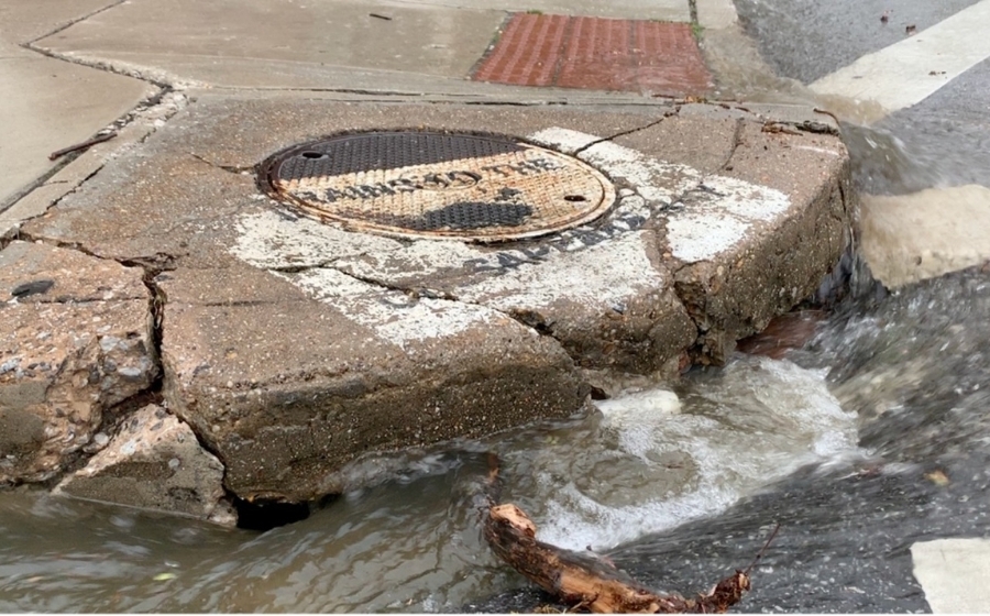 water rushes into a stormwater drain at a street corner