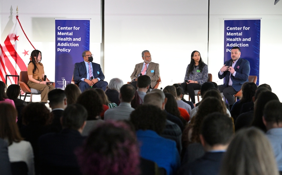 Five adults seated on venue stage with microphone in hand.
