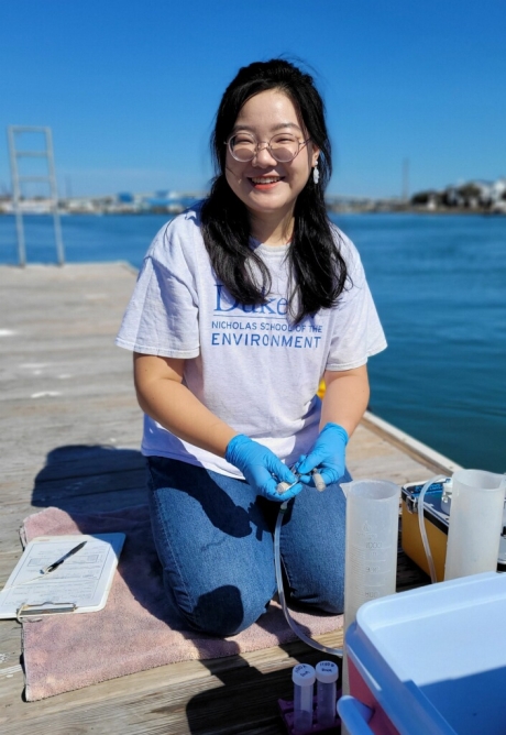 Female kneeling on a dock with test tubes and testing equipment