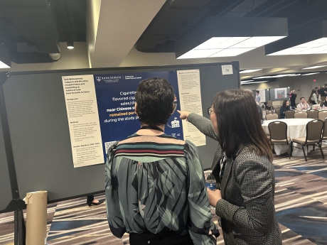 A woman in a dark blazer shares her research with a woman in a colorful top