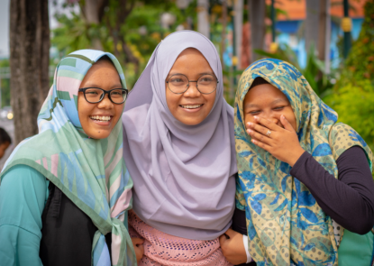 Three teenage girls wearing hijabs, standing outside and laughing 