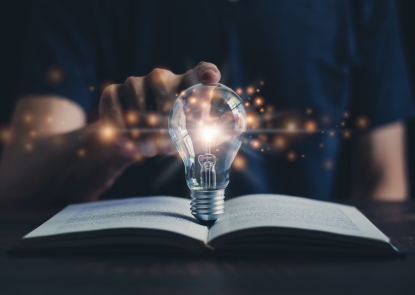 person putting a finger on top of a lightbulb that's on an open book