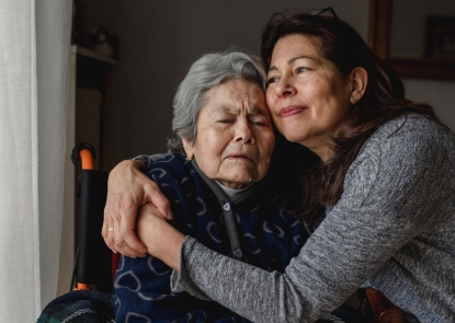 An middle-aged adult hugging an elderly adult