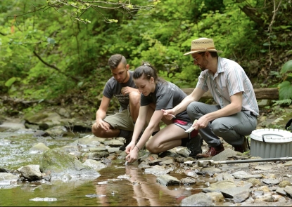 man in hat, young man and young woman take samples from a creek
