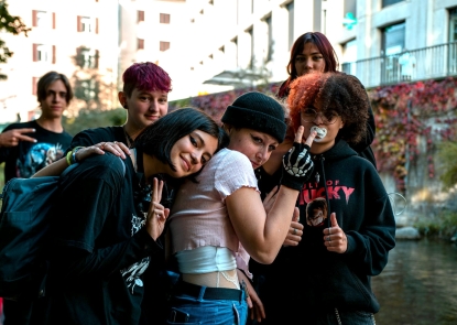 A group of six teenagers smiling in front of a spray painted wall 