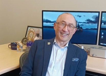 A man in a suit jacket and collared shirt sitting in front of desk