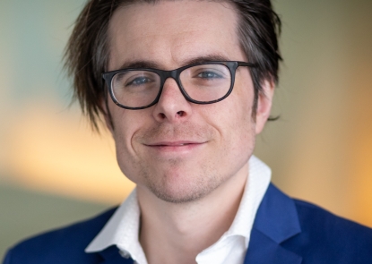 A headshot of Danny Scerpella, a man with a light skin tone, short dark hair, and black glasses