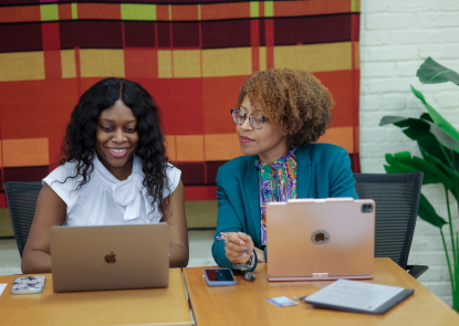 Two women sitting next to each other looking at the same laptop
